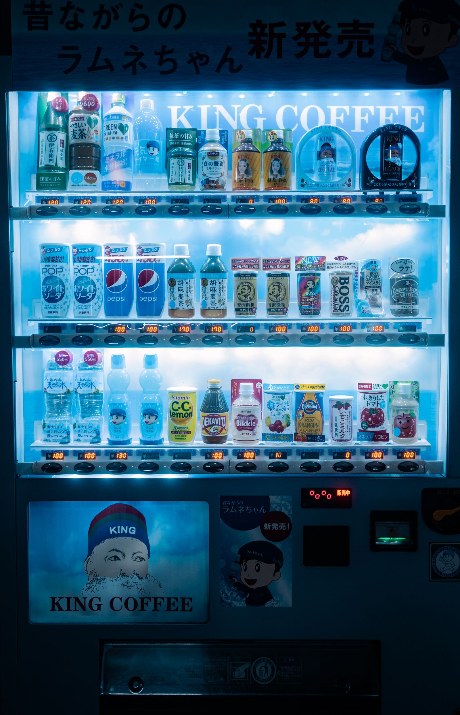 Illuminated cold-drink vending machine stocked with bottled and canned beverages